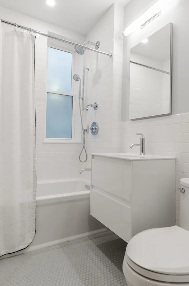 White minimalist bathroom with a bathtub/shower combo, frosted window, and a wall-mounted vanity with mirror; compact and bright.